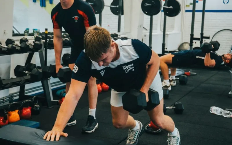Men lifting dumbbells during a workout session in a gym. Strength and fitness training.