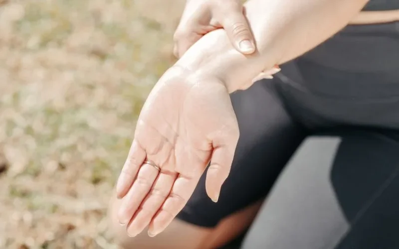 Person gripping wrist in pain, highlighting injury and support outdoors.