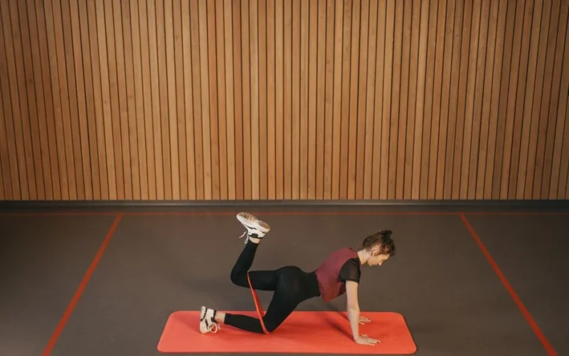Woman performing a resistance band workout on a mat indoors, focusing on fitness and strength.