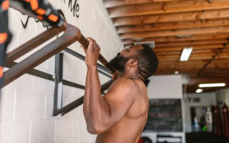 A shirtless man doing a pull-up exercise on a pull-up bar.
