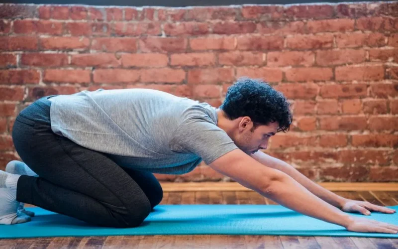 Side view of focused male doing Uttana Shishosana to stretch spine and shoulders during yoga session