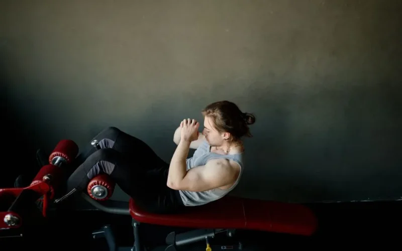 Focused young man doing abdominal exercises on a gym bench.