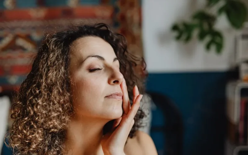 A relaxed woman with curly hair enjoying a skincare routine indoors.