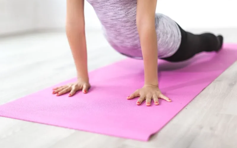 A woman performs a yoga stretch indoors on a pink mat, promoting a healthy lifestyle.