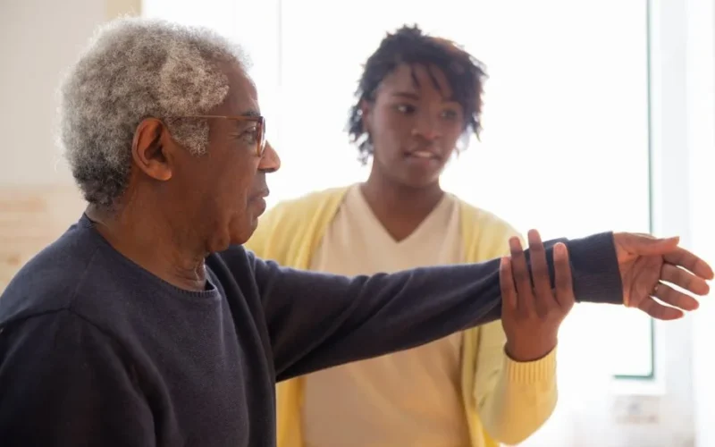 A caregiver helps an elderly man with arm exercises in a warm and caring environment.