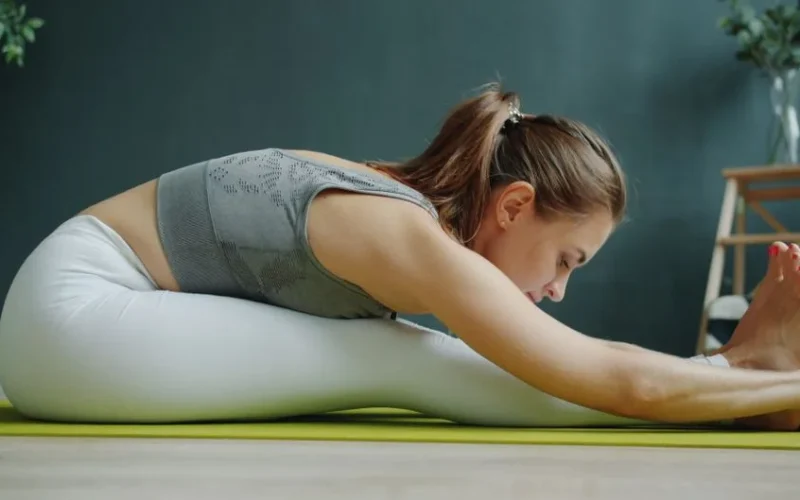 A woman in activewear stretching on a yoga mat indoors, focusing on wellness and fitness.