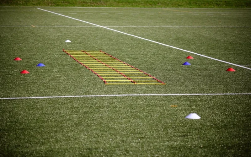 Agility ladder and marker cones set up on a grassy football field for training.