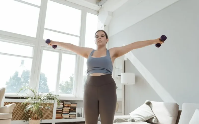 Determined young woman in activewear lifting dumbbells indoors for fitness.