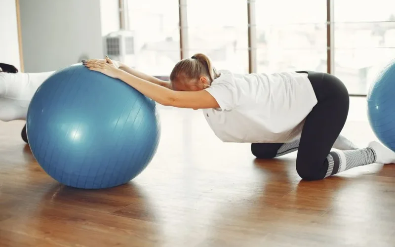 Side view of female sportswoman while group training with fitness ball during prenatal workout with crop friend in modern gym during daytime