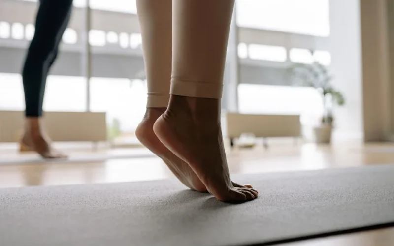 Detail shot of bare feet balancing on a yoga mat inside a bright studio.