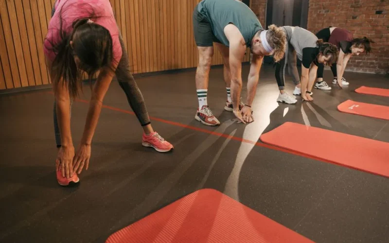 A diverse group of adults stretching on mats during a gym workout session.