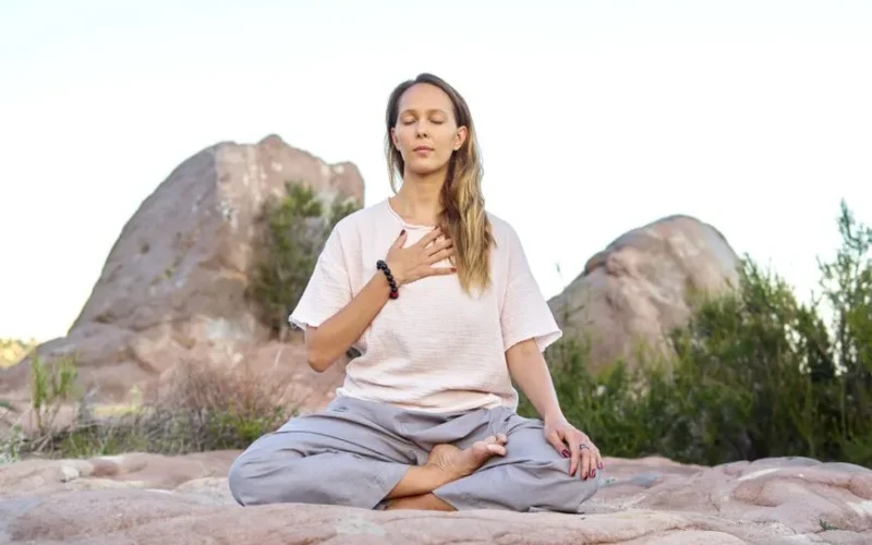 Woman meditating outdoors with closed eyes, embodying peace and relaxation.