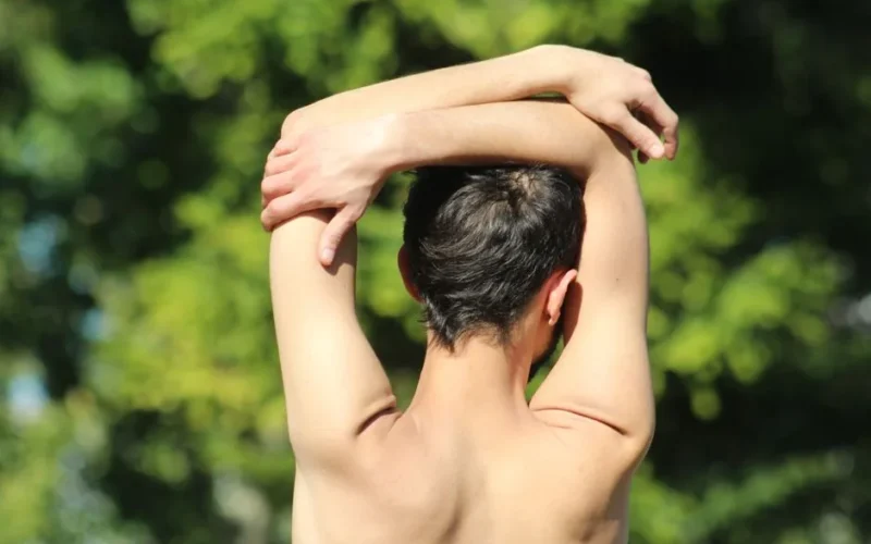 Man performs back stretching exercise on a sunny day, promoting wellness and fitness.
