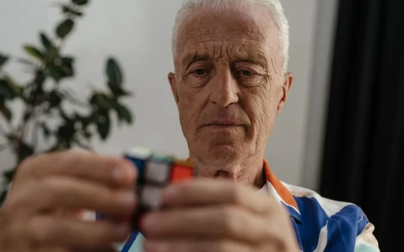 Elderly man concentrating on solving a Rubik's Cube, showcasing focus and mental agility.