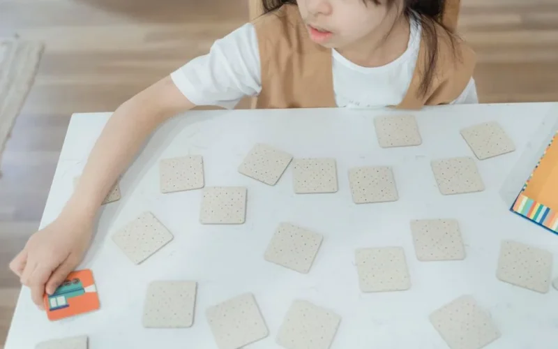 Young child playing a memory card game on a white table. High-angle view indoors.