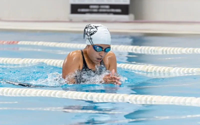 Adult woman swimming breaststroke during competition in indoor pool.