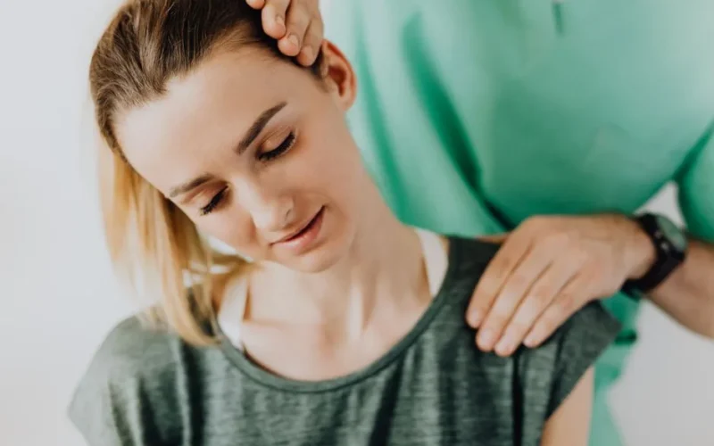 Crop professional male massage therapist in green medical uniform doing therapeutic neck massage on content female patient wearing casual clothes