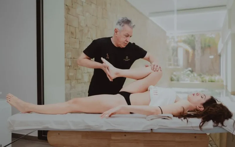 A therapist assists a patient during a rehabilitation session indoors, promoting mobility and flexibility.