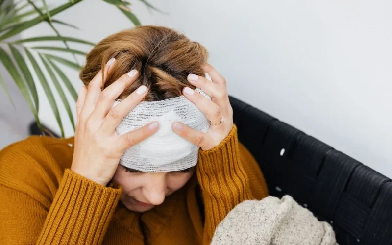 Woman with head injury holding her head in pain indoors.