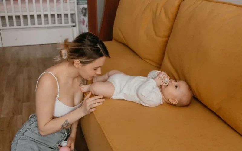A mother sitting beside her baby on a couch, enjoying a tender moment indoors.