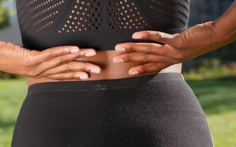 Close-up of a woman's hands gripping her painful back while outdoors.