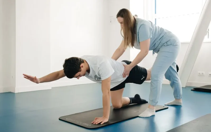 A physiotherapist guides a patient's exercise on a mat in a Vilnius gym.