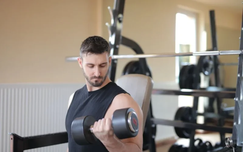 Adult male exercising with dumbbell in a gym, showcasing bicep strength training.