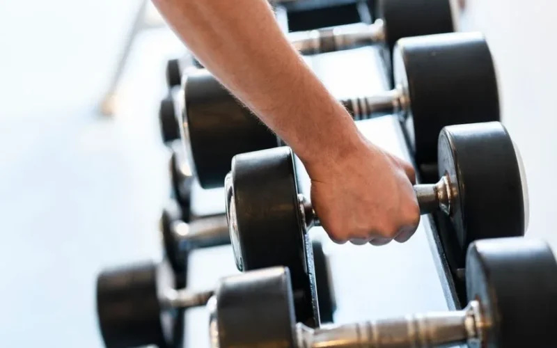 Close-up of a man's hand gripping a dumbbell in an indoor gym setting.
