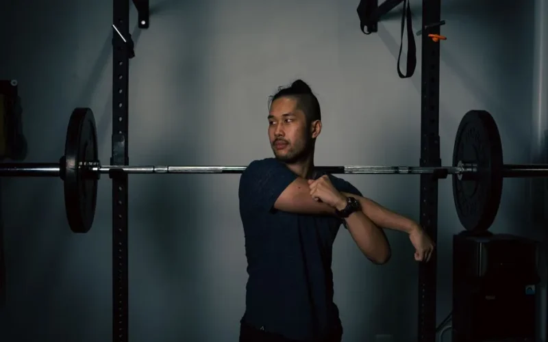 Man stretching near barbell equipment in a home gym, preparing for workout.