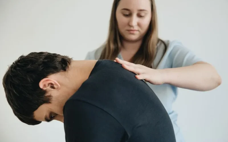 A physiotherapist assisting a patient with back pain in an indoor clinic setting.