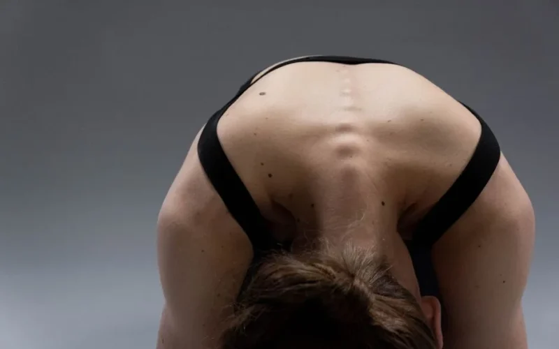 A woman performing a yoga pose that highlights her flexible back muscles in a studio setting.