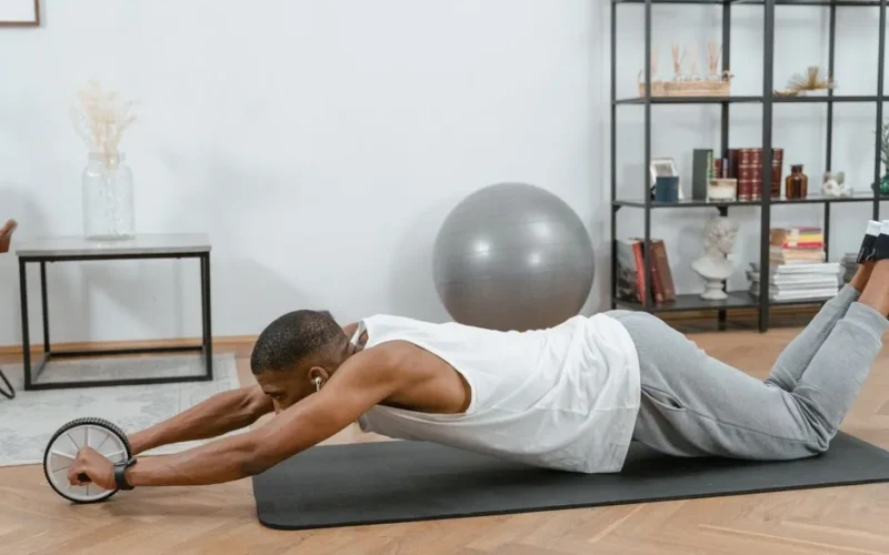 Man using an ab roller on a yoga mat indoors, promoting fitness and healthy lifestyle.