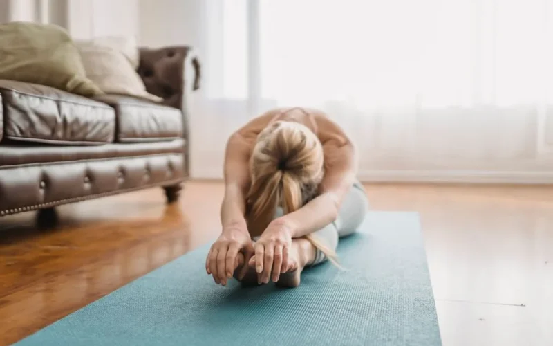 Full body of anonymous female yogi in sportswear doing Seated Forward Bend stretching asana during yoga practice in living room