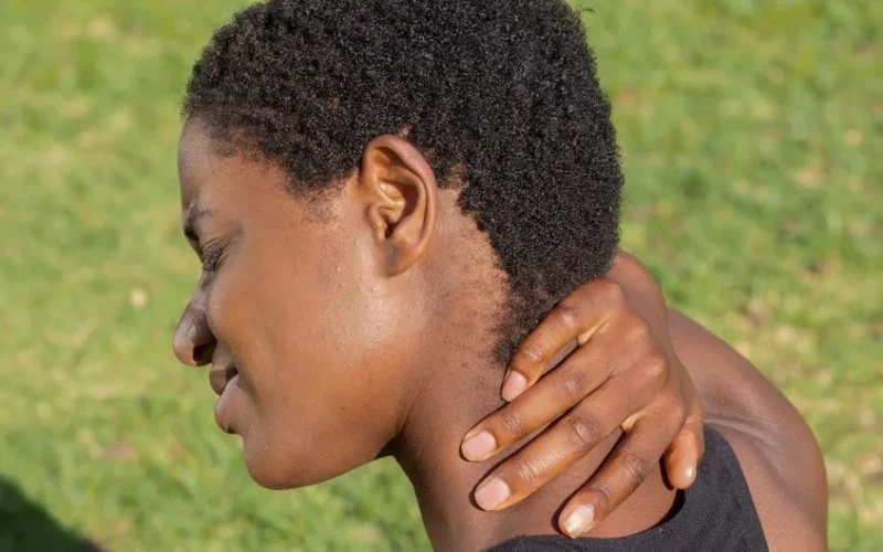 African American woman touching neck outdoors, experiencing discomfort.