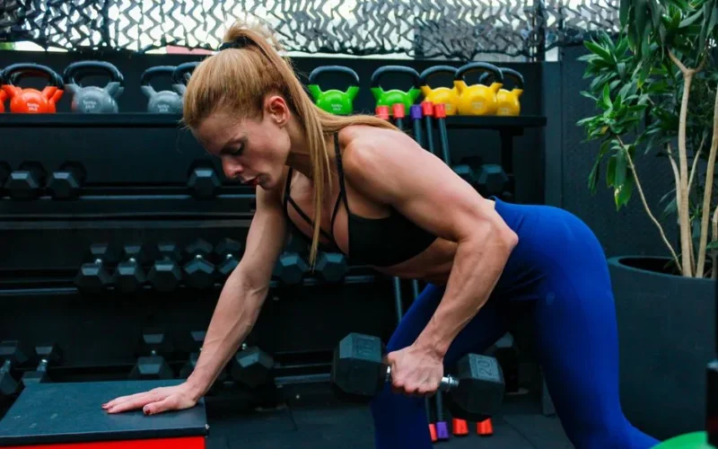 Woman exercising with dumbbells in gym. Focused on strength training and fitness.