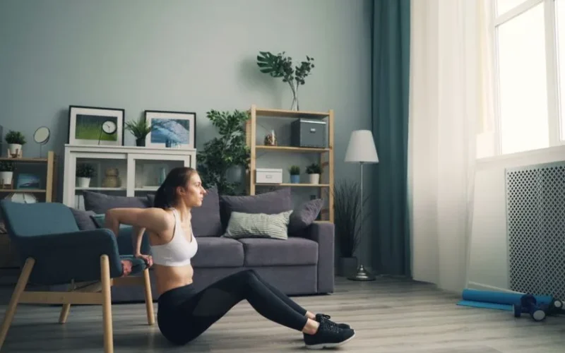 Woman doing tricep dips at home using a chair for support, promoting fitness indoors.