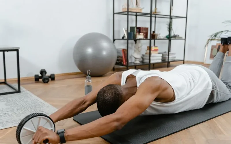 A man performs an ab roller workout indoors, emphasizing healthy lifestyle and fitness.