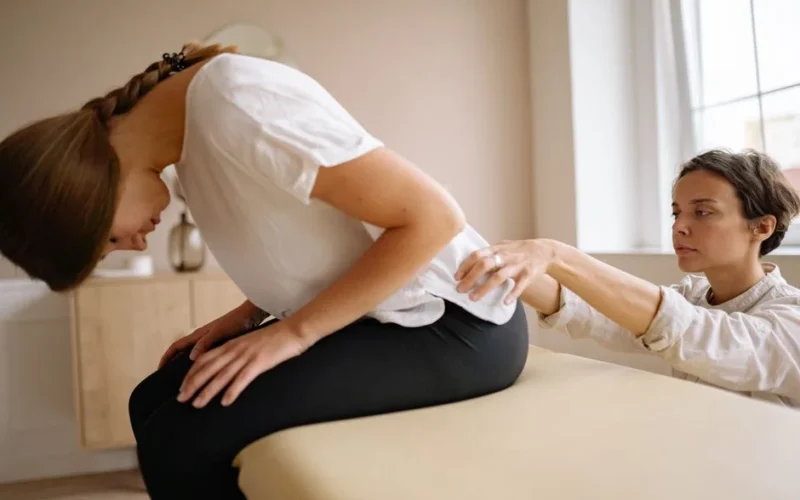 A therapist stretches a patient's back during a physical therapy session indoors.