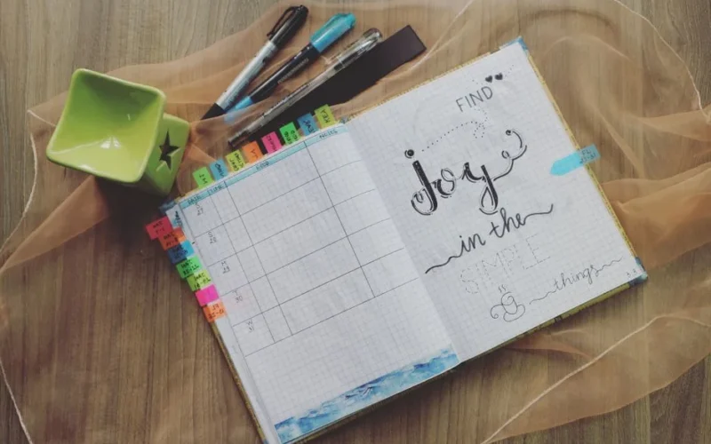 Flat lay of an open bullet journal with pens on a wooden desk, expressing creativity and planning.