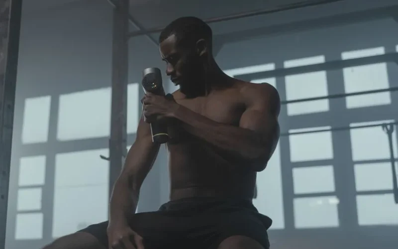 A dedicated athlete uses a massage gun to relax his muscles post-workout in the gym.