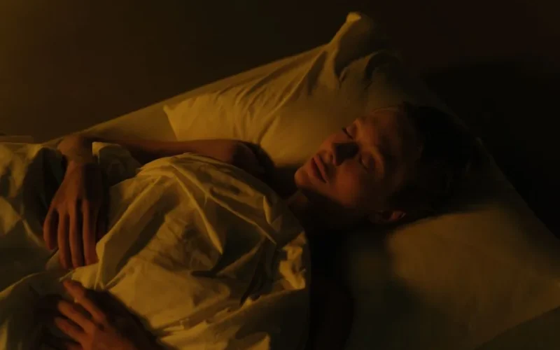 A woman peacefully sleeping in a dimly lit bedroom, wrapped in a white blanket.