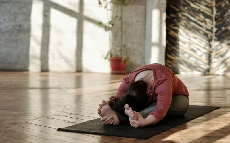 A woman stretches on a yoga mat in a sunlit room, embracing relaxation and wellness.
