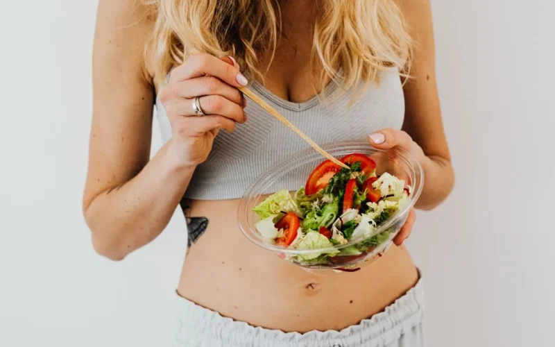 Woman in sports attire enjoys a fresh, nutritious salad, embodying a healthy lifestyle.