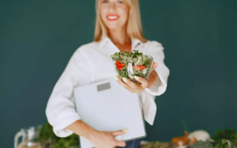 A woman with a vibrant smile offering a fresh salad bowl, promoting healthy eating.