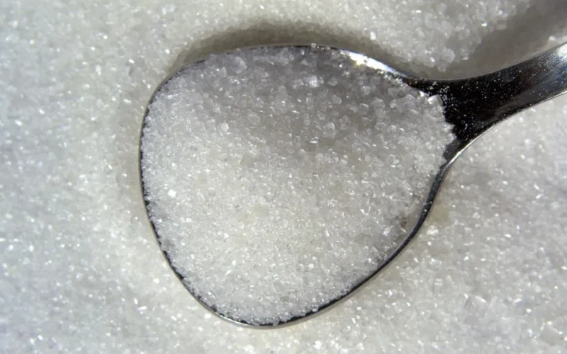 Detailed macro shot of white sugar crystals on a reflective spoon.