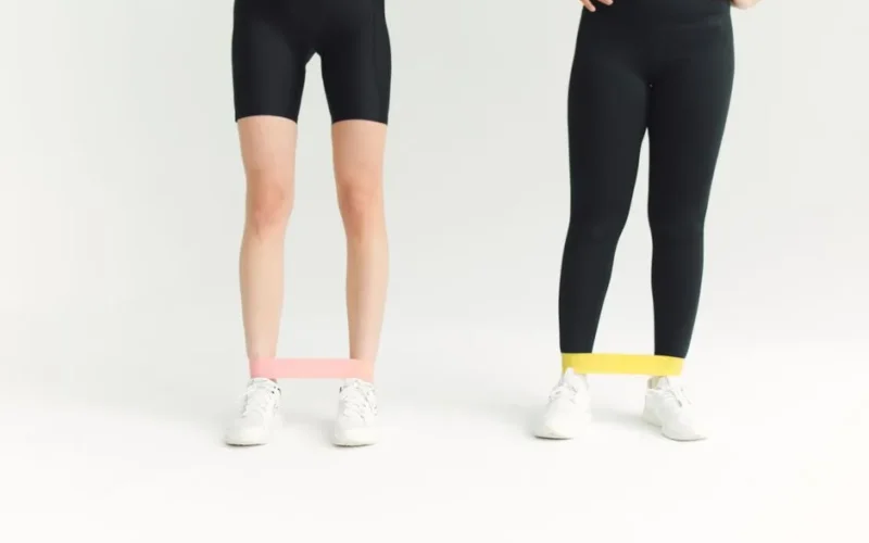 Two women in activewear using resistance bands during an indoor workout session.