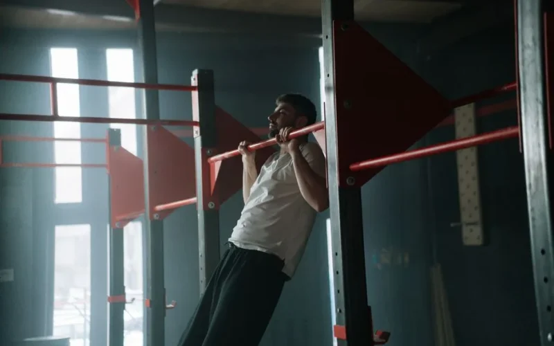 Adult man doing pull-ups in a dimly lit indoor gym, focused on upper body training.