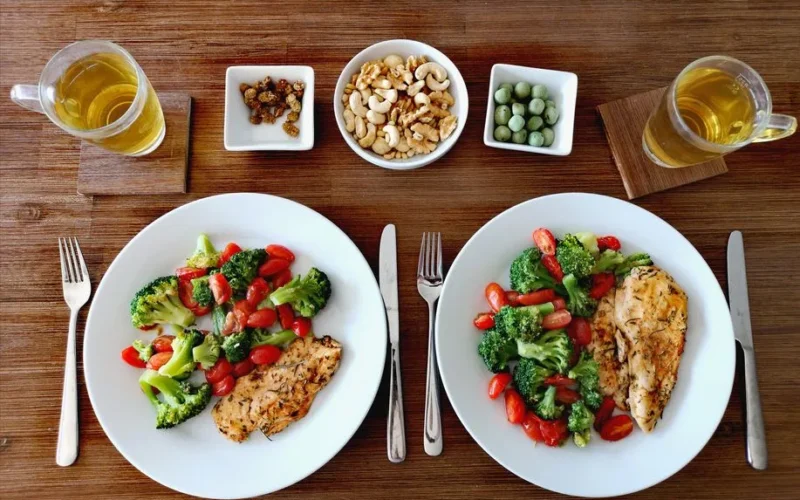 A delicious and healthy chicken dinner with fresh vegetables, nuts, and tea in a cozy setting.