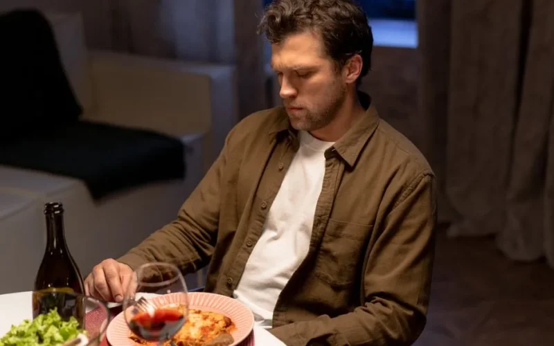 Man seated at dinner table with wine, lasagna, and salad, appearing thoughtful.