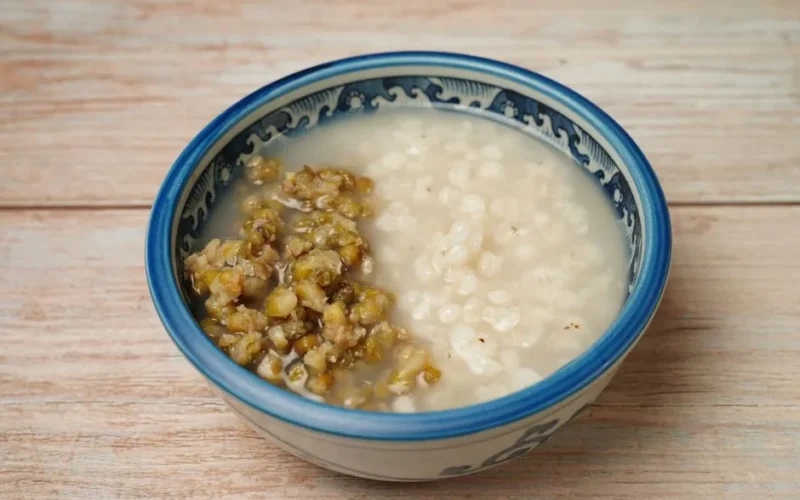 A close-up of mung bean and rice porridge served in an ornate blue and white ceramic bowl on a wooden surface.